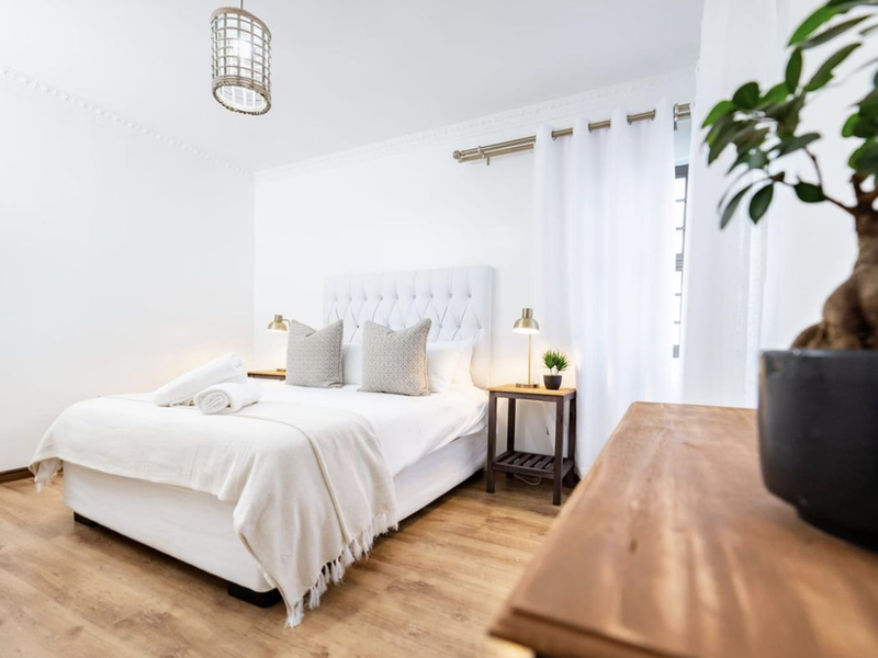 A bright and well-maintained bedroom featuring light-toned laminate flooring, decorative ceiling cornicing, and a modern pendant light fixture.