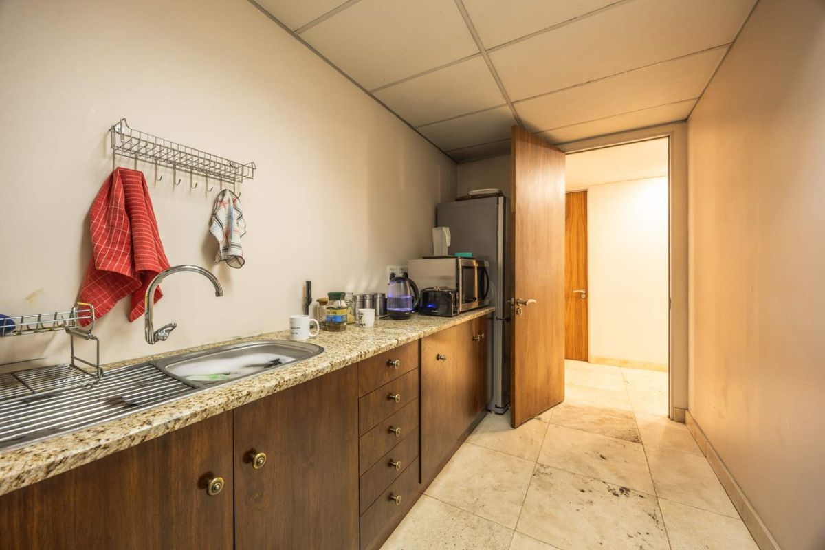 A functional office kitchenette featuring granite countertops, stainless steel sink, and built-in wooden cabinetry with tiled flooring.