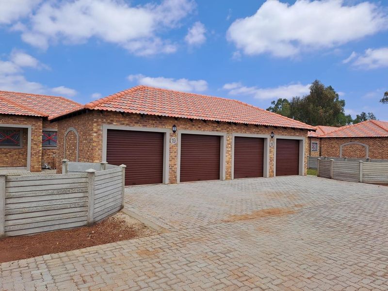 A well-maintained exterior view of a four-car garage block featuring brick construction, tiled roofing, and a paved driveway area.