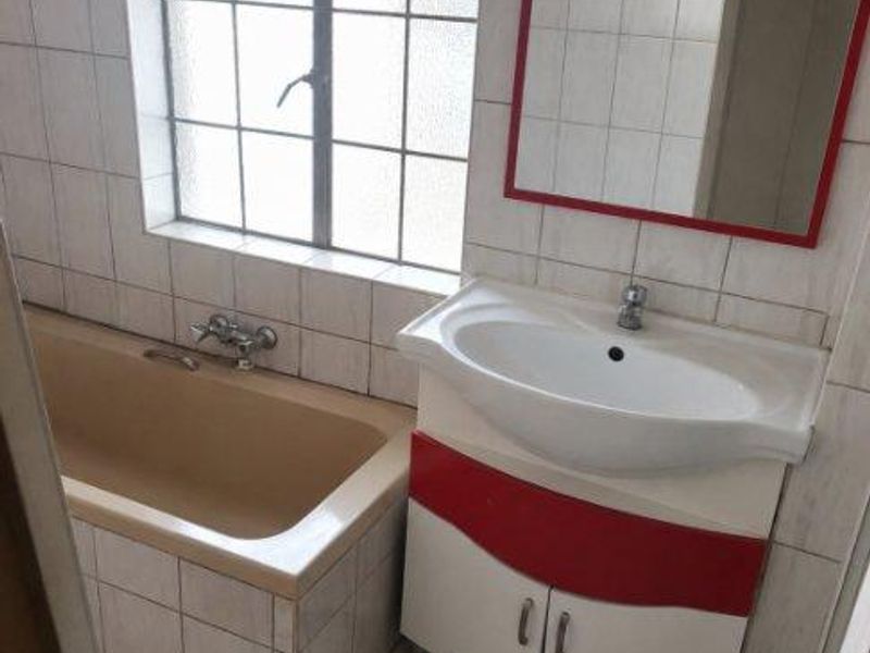 A dated bathroom featuring a built-in bathtub, tiled surfaces, and a vanity basin unit with a wall-mounted mirror.