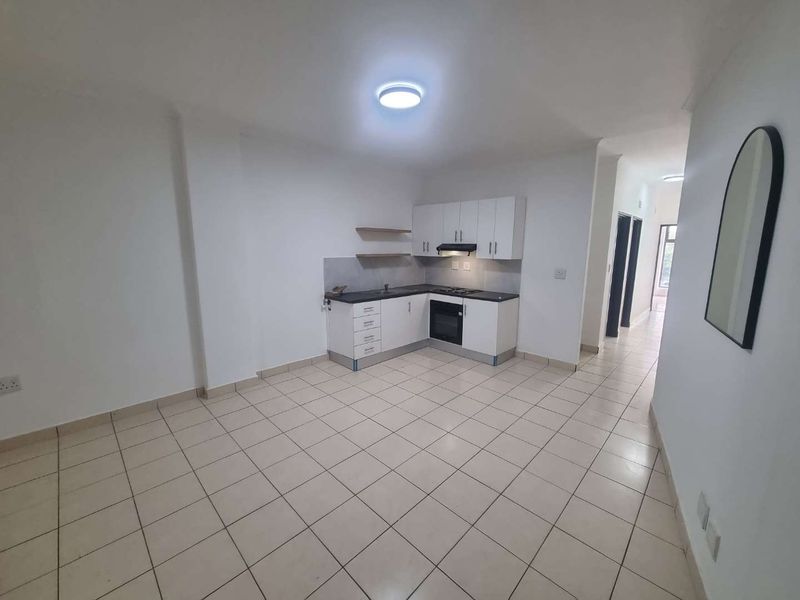 An open-plan living and kitchen area featuring tiled flooring, white cabinetry, and built-in cooking appliances in a clean, vacant space.