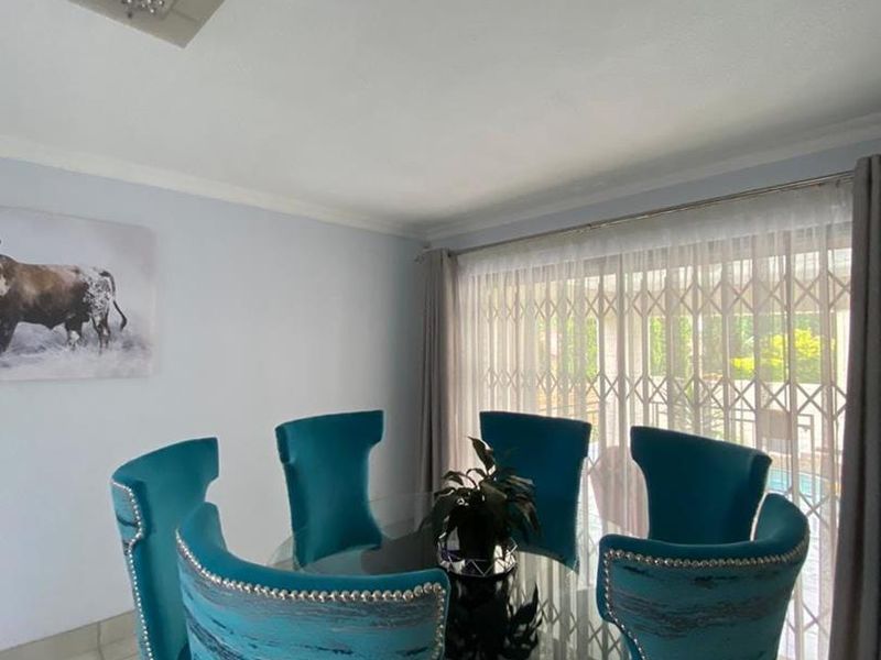 A bright dining room featuring tiled flooring, coved ceilings, and a large sliding glass door with a security gate leading to the exterior.