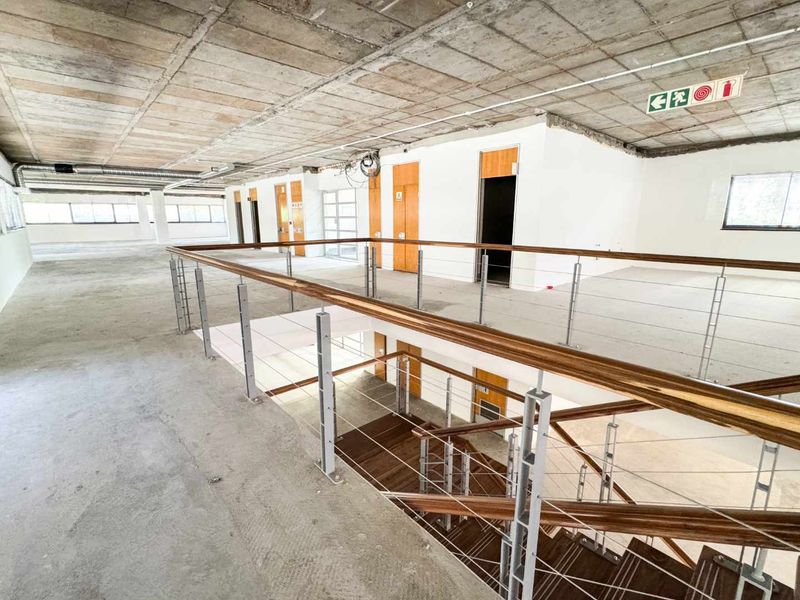 Expansive open-plan commercial space featuring an industrial aesthetic with exposed concrete ceilings, a central staircase, and multiple access doors.