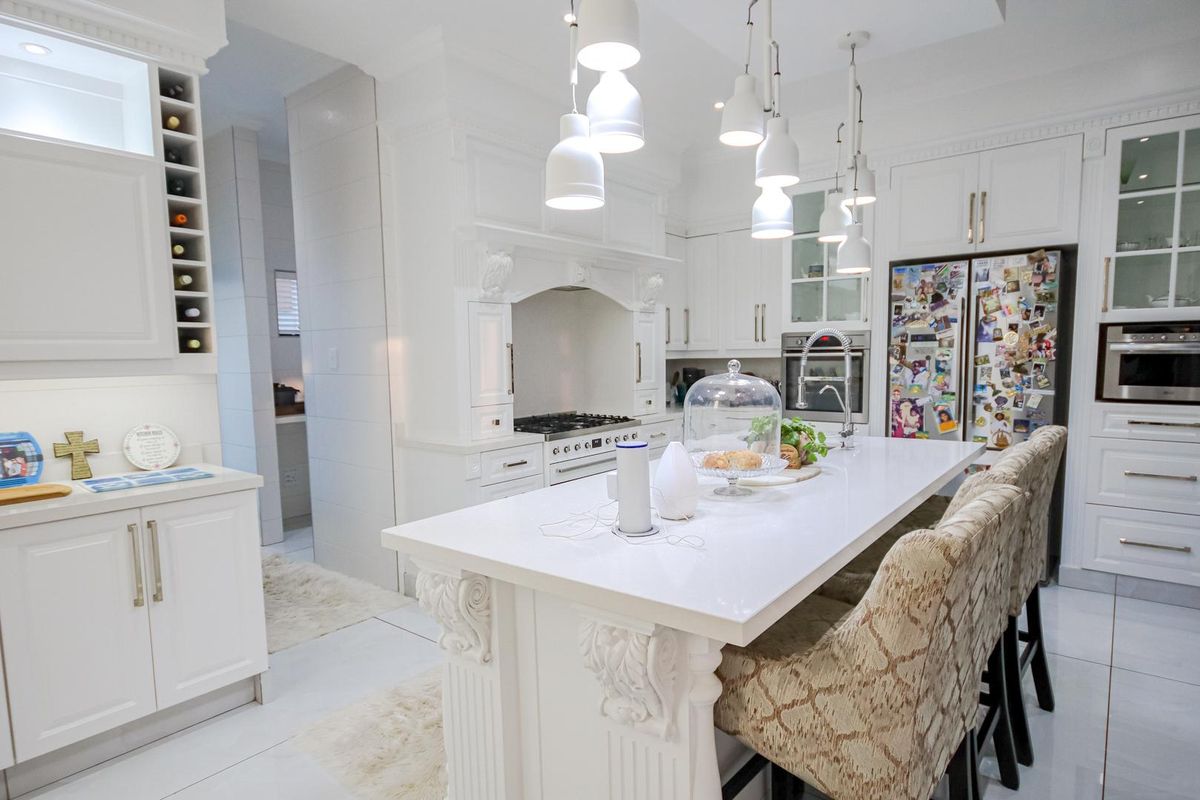 A bright, modern kitchen featuring white cabinetry, a large central island with stone countertop, integrated appliances, and elegant pendant lighting.