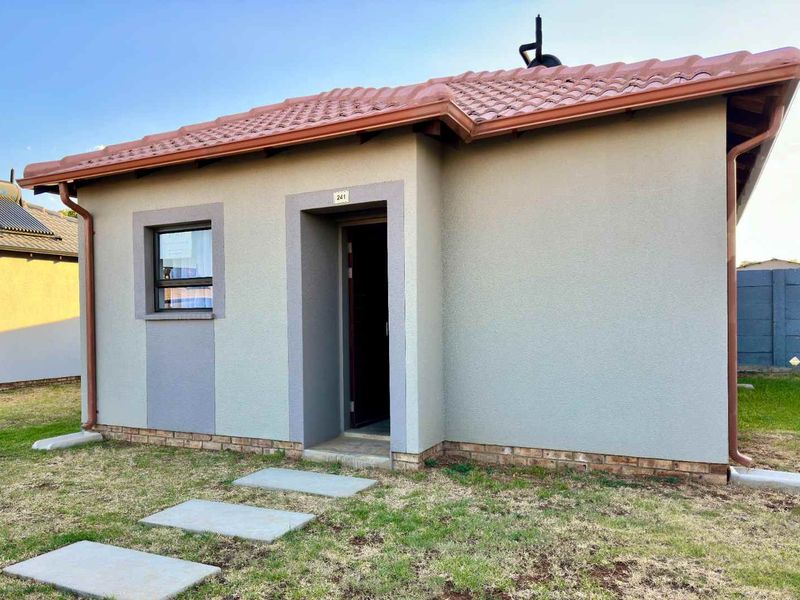 A well-maintained single-story residential exterior featuring a tiled roof, plastered walls, and a paved walkway leading to the front entrance.