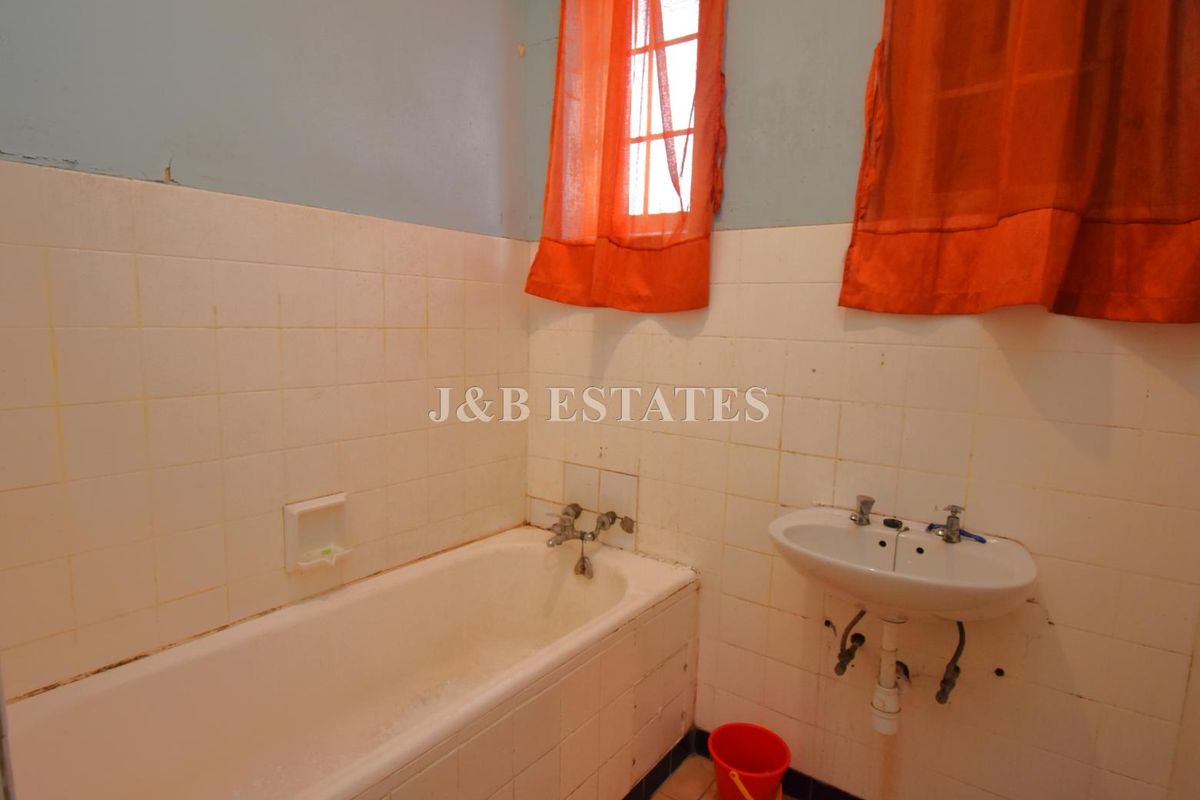 A dated bathroom featuring a standard bathtub, wall-mounted basin, and tiled walls, requiring cosmetic updates and maintenance.