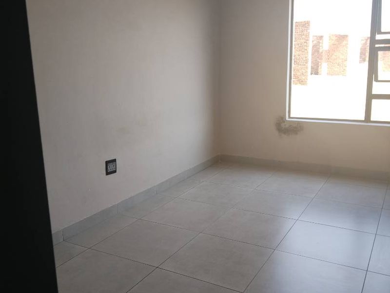 An empty bedroom featuring neutral tiled flooring and a large window, providing a blank canvas for personalization.