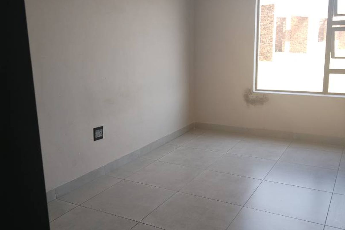 An empty bedroom featuring neutral tiled flooring and a large window, providing a blank canvas for personalization.