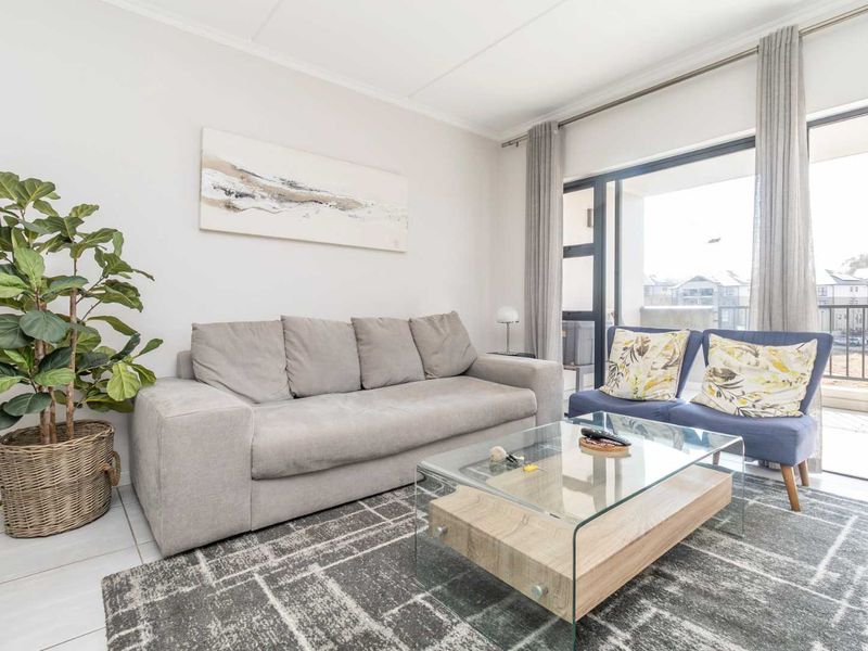 A bright and well-maintained living room featuring tiled floors and a large sliding glass door providing access to an outdoor balcony area.
