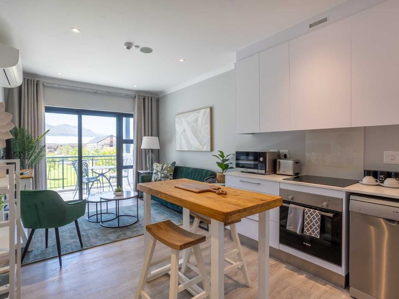 Modern open-plan apartment featuring a sleek kitchen with built-in appliances, flowing into a living area with direct access to a private balcony.