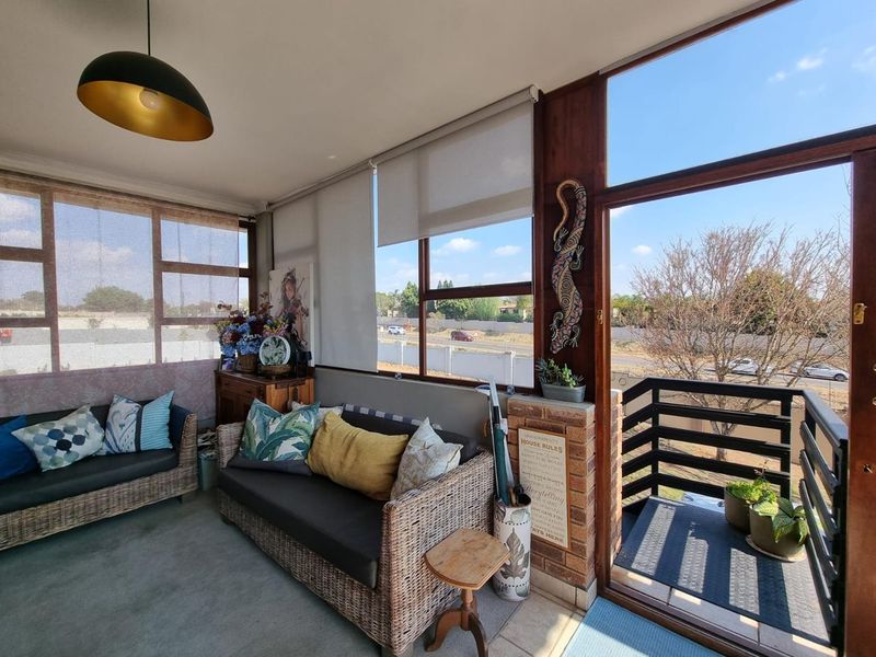 Enclosed balcony area featuring large windows, roller blinds, and a metal railing, providing a bright and airy space with outdoor views.