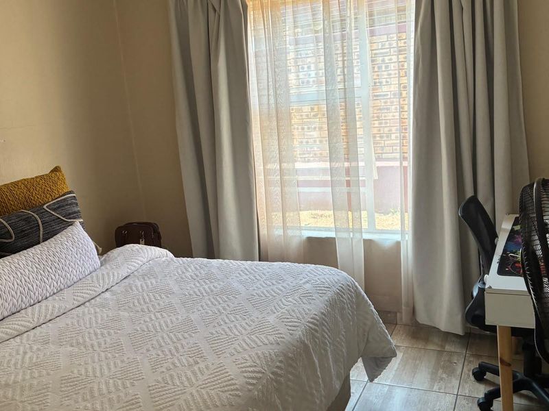 A functional bedroom featuring tiled flooring and natural light through a window with curtain tracks.