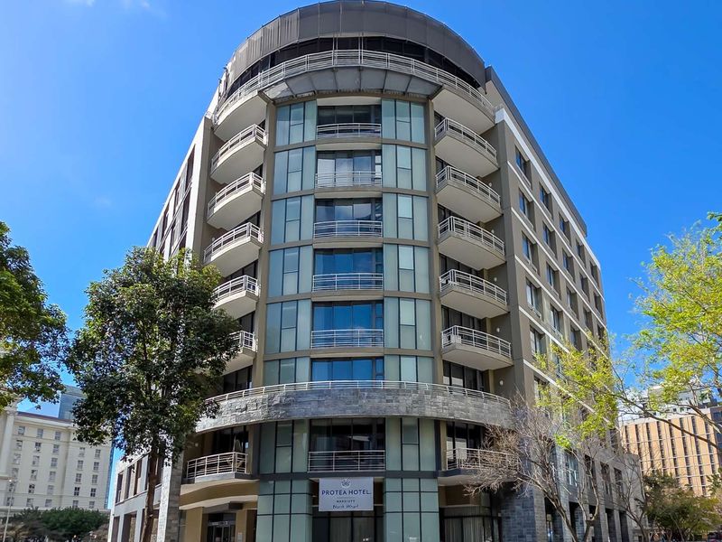 A modern multi-story apartment building featuring a curved facade, glass curtain walls, and private balconies with metal railings.