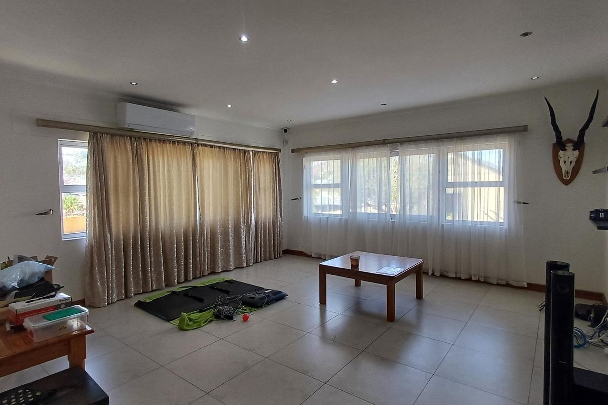 Spacious living room featuring tiled flooring, recessed downlighting, and a wall-mounted split-system air conditioner, offering a bright and functional living space.