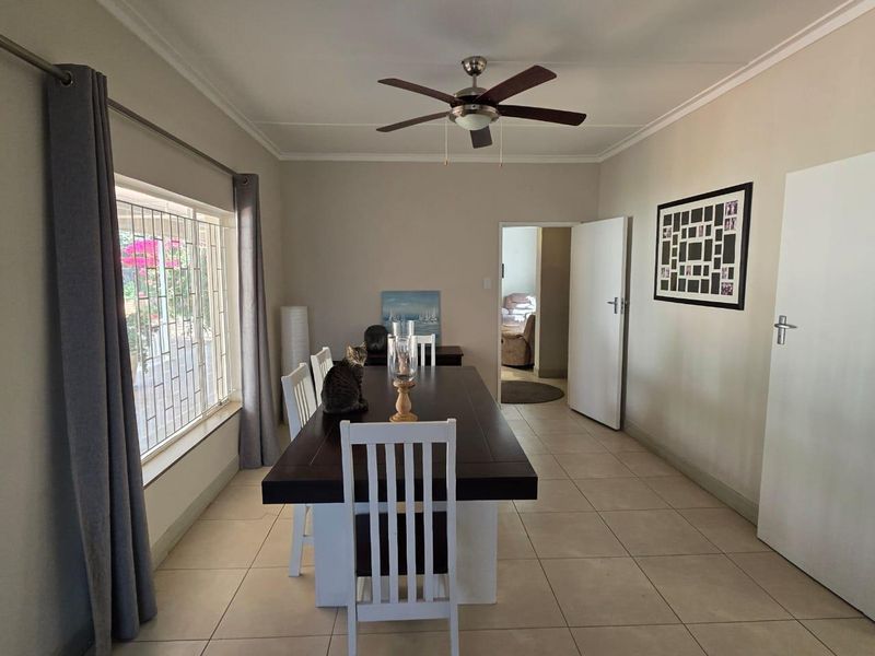 A functional dining room featuring tiled flooring, a ceiling fan, and large windows with security bars, providing a bright and practical space for meals.