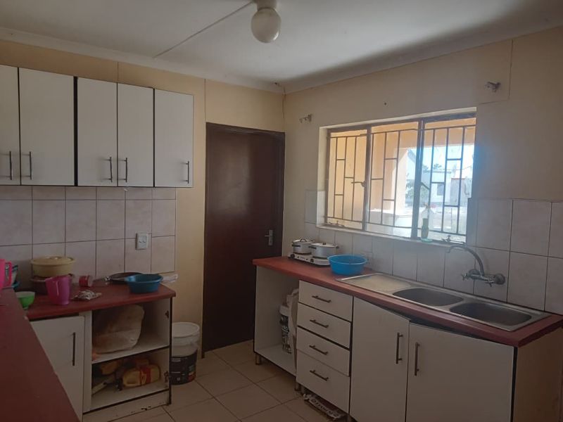 A functional kitchen featuring built-in cabinetry, laminate countertops, a double bowl sink, and tiled splashbacks, requiring cosmetic updates to improve its overall condition.
