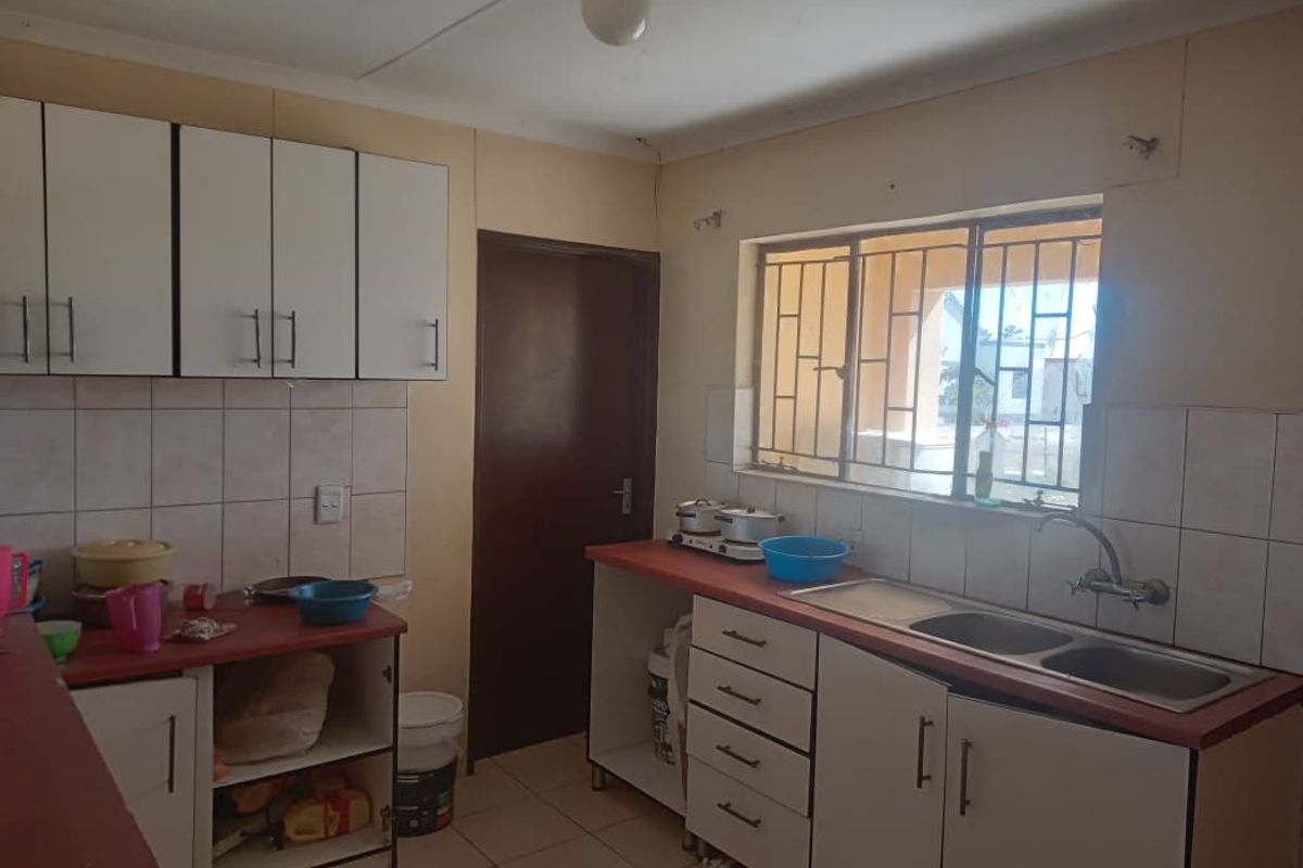 A functional kitchen featuring built-in cabinetry, laminate countertops, a double bowl sink, and tiled splashbacks, requiring cosmetic updates to improve its overall condition.