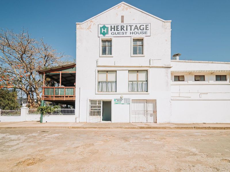 Front elevation of the Heritage Guest House featuring a gabled facade, timber balcony, and security gates, showing signs of weathered exterior paint and plaster.