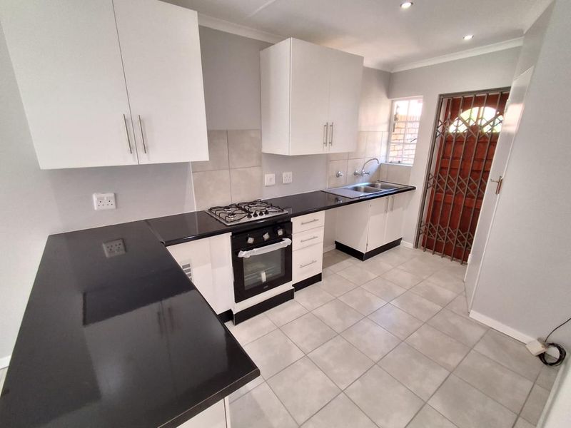 A clean, modern kitchen featuring white cabinetry, black countertops, a gas hob, built-in oven, and tiled flooring with direct access to an exterior door.