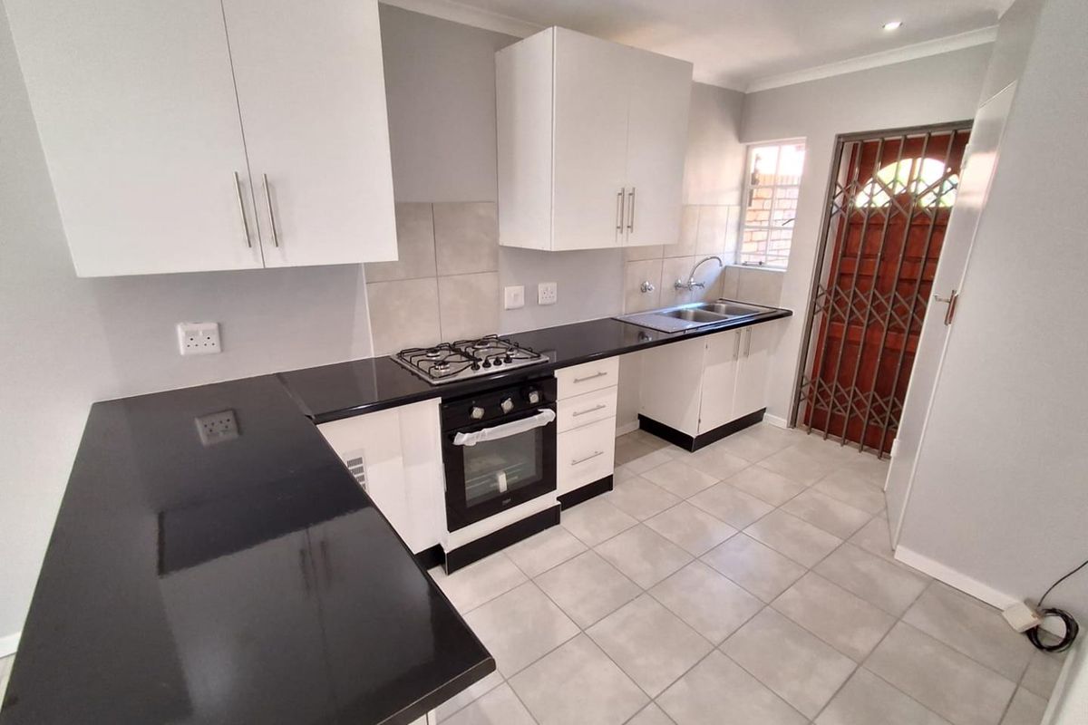 A clean, modern kitchen featuring white cabinetry, black countertops, a gas hob, built-in oven, and tiled flooring with direct access to an exterior door.