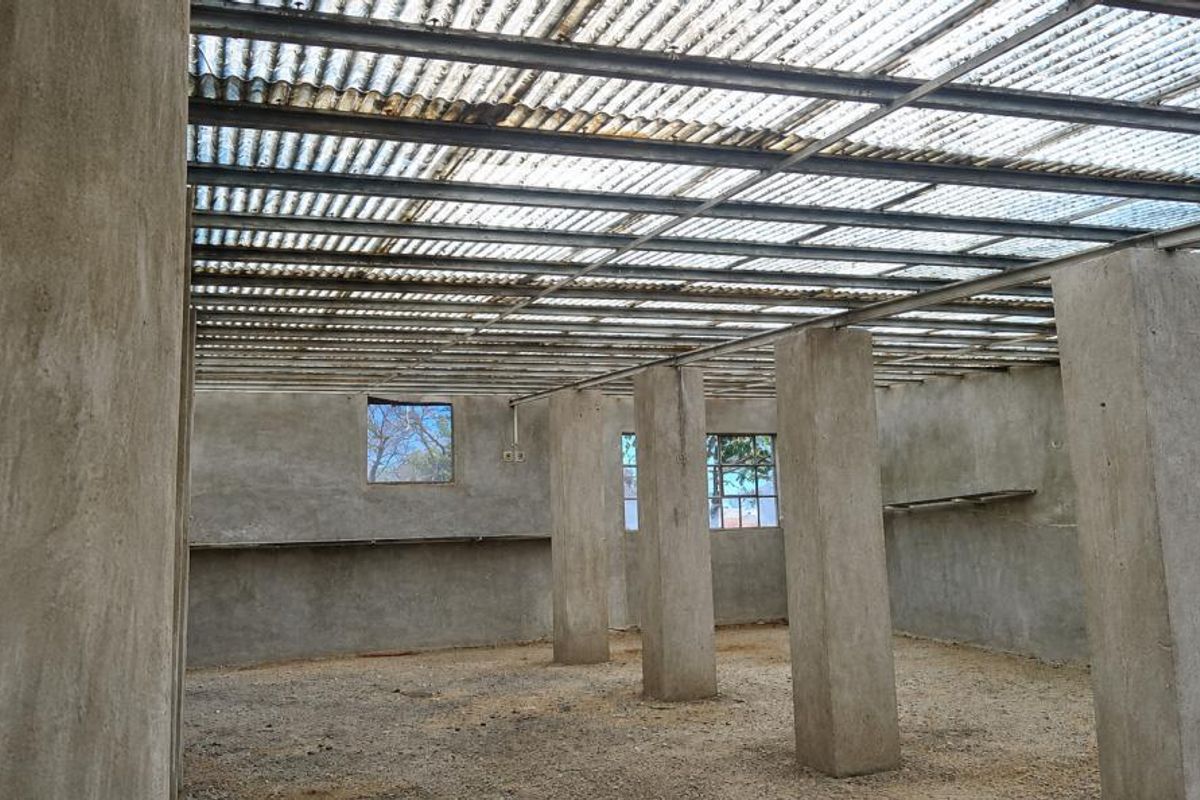 An unfinished utility space featuring concrete columns, exposed steel roof structure with translucent sheeting, and raw cement plastered walls.