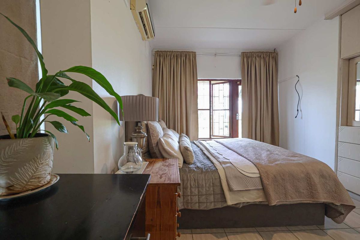 A bedroom featuring tiled flooring, built-in cupboards, and a wall-mounted air conditioning unit, with direct access to an outdoor area.