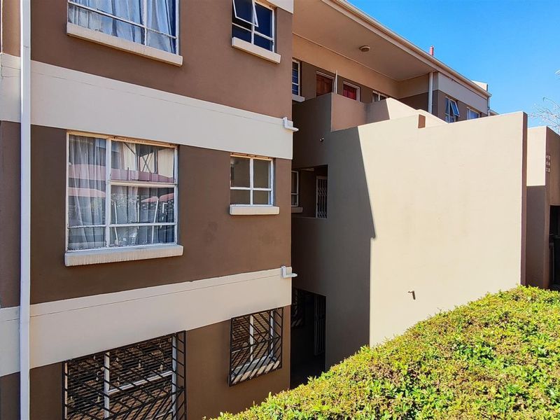 Rear elevation of a multi-story townhouse complex featuring plastered walls, aluminium window frames with security bars, and an integrated balcony structure.