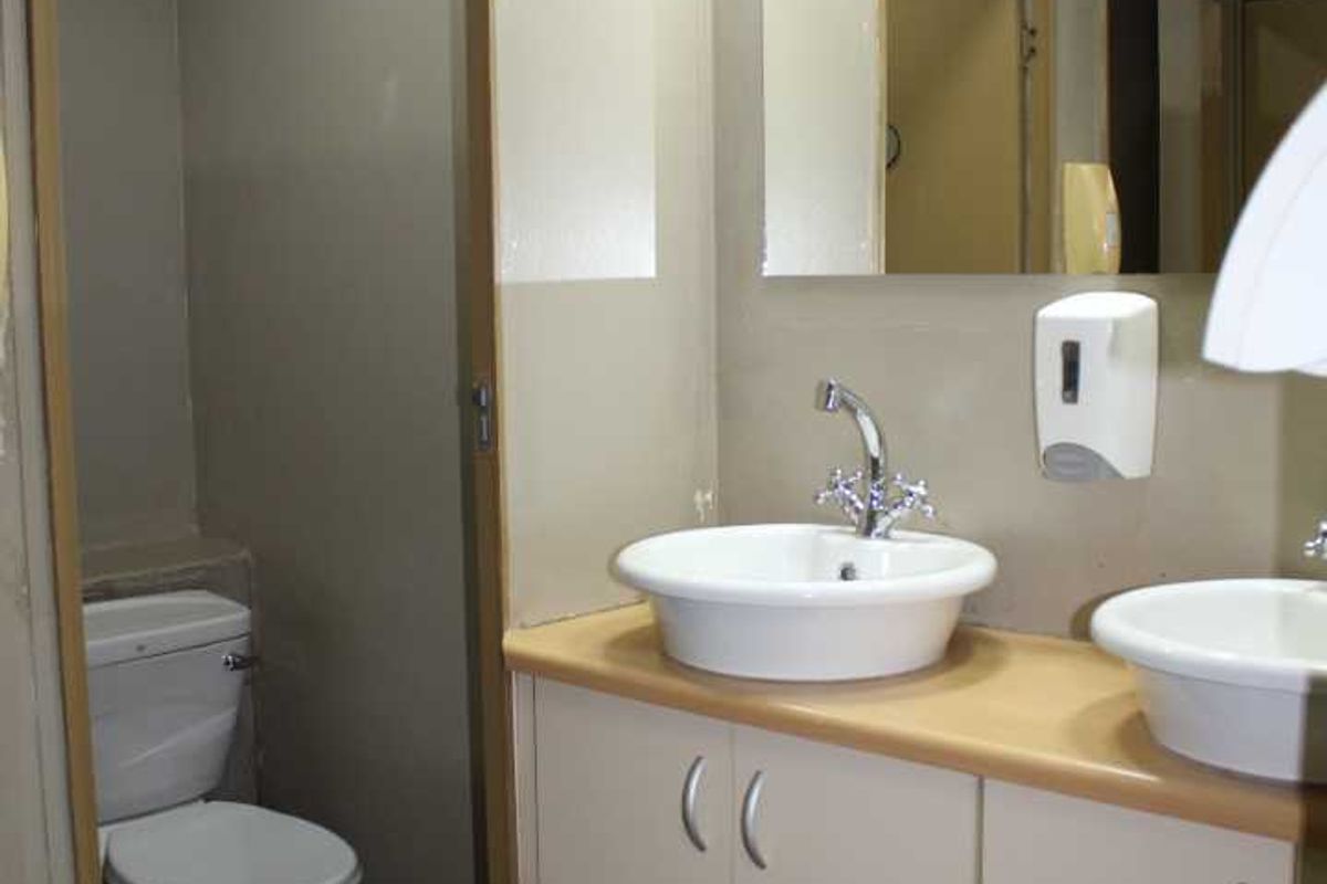 A functional office restroom featuring dual vessel sinks, built-in vanity cabinetry, a wall-mounted mirror, and a separate toilet cubicle.