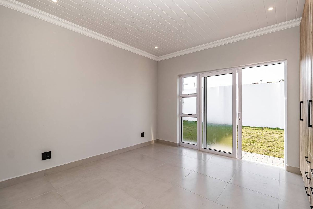 A bright, empty bedroom featuring tiled floors, built-in cupboards, and a sliding glass door providing direct access to the rear garden.