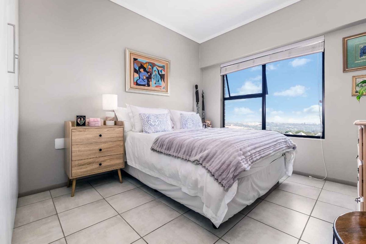 A bright and well-maintained bedroom featuring large windows with expansive views, neutral tiled flooring, and built-in wardrobe storage.