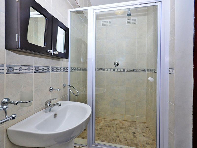 A functional bathroom featuring a pedestal washbasin, a glass-enclosed shower, and wall-mounted cabinetry with neutral tiled finishes.