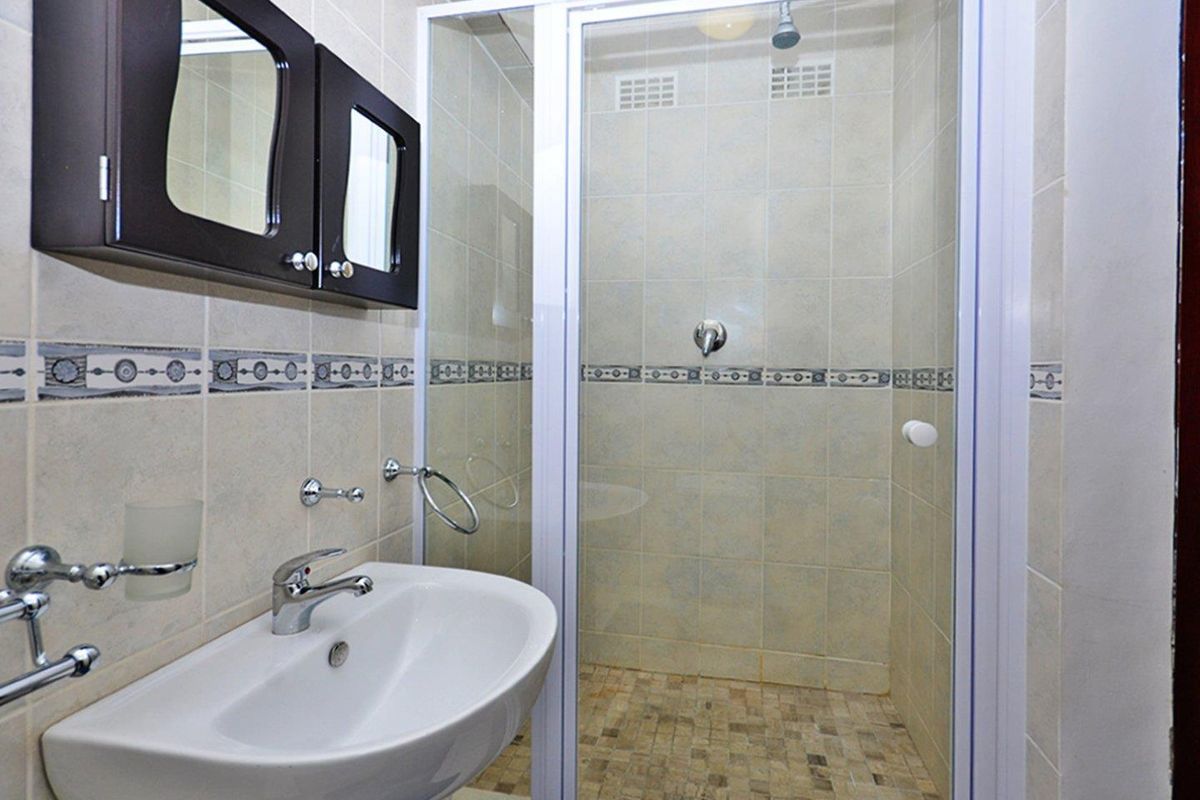 A functional bathroom featuring a pedestal washbasin, a glass-enclosed shower, and wall-mounted cabinetry with neutral tiled finishes.
