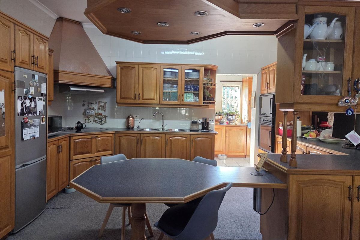 A traditional kitchen featuring extensive timber cabinetry, a built-in oven, extractor fan, and a central breakfast nook, with an adjoining scullery area.