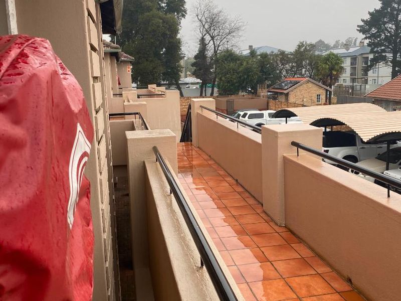 A long, tiled balcony with metal balustrades, overlooking the complex parking area and surrounding neighborhood.