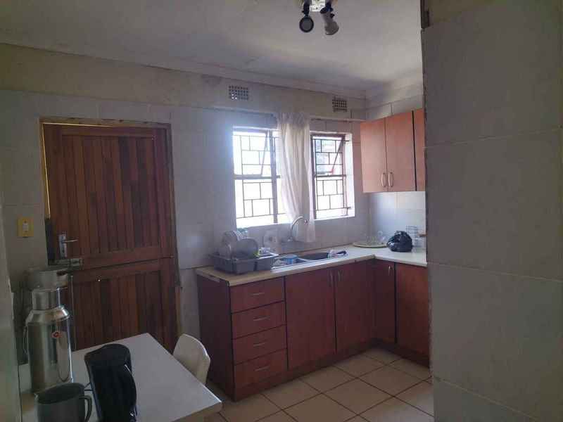 A dated kitchen featuring laminated cabinetry, tiled splashbacks, and tiled flooring, with direct access to an exterior door.