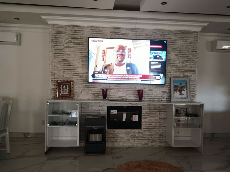 A living room featuring a stone-clad feature wall with built-in cabinetry, recessed ceiling lighting, and tiled flooring.