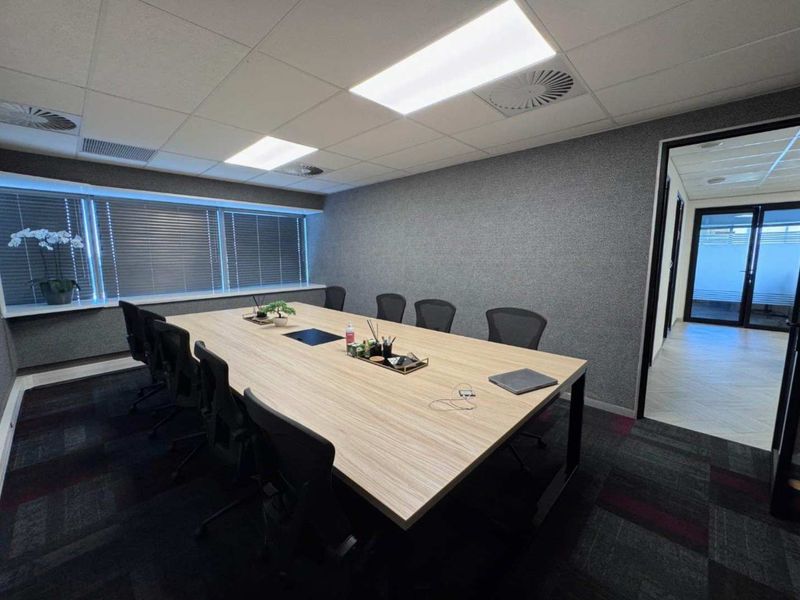 A professional office boardroom featuring a large meeting table, suspended ceiling with recessed lighting, and carpeted flooring.