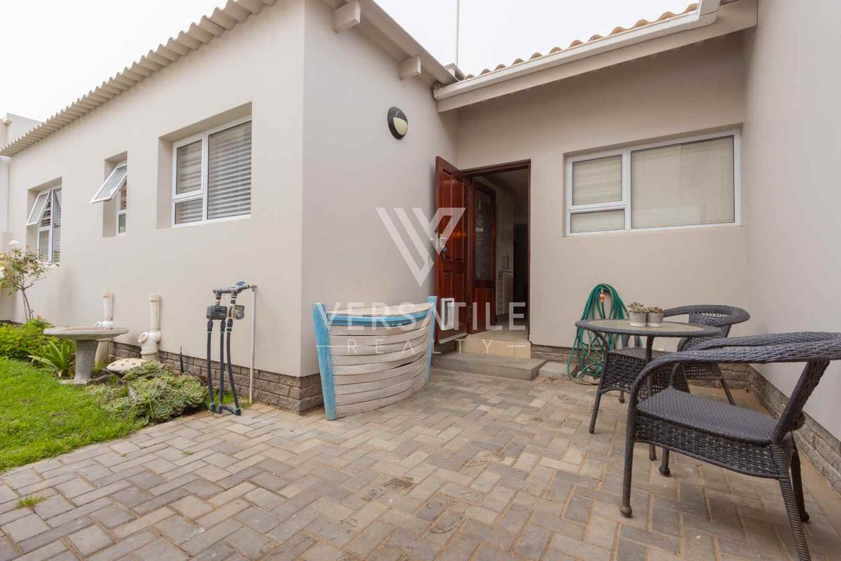 A paved rear patio area featuring a brick-paved surface, exterior wall lighting, and access to the interior through a standard door.