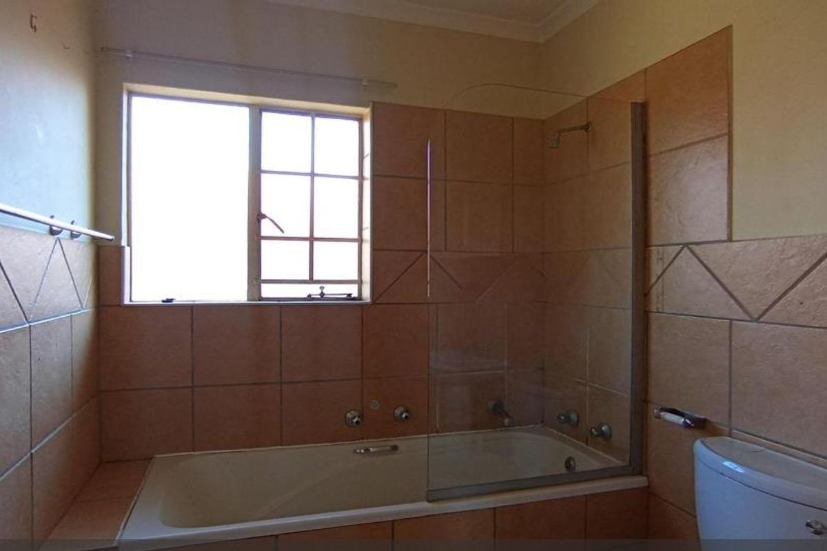 A functional bathroom featuring a built-in bathtub with a glass shower screen, tiled walls, and a standard toilet.