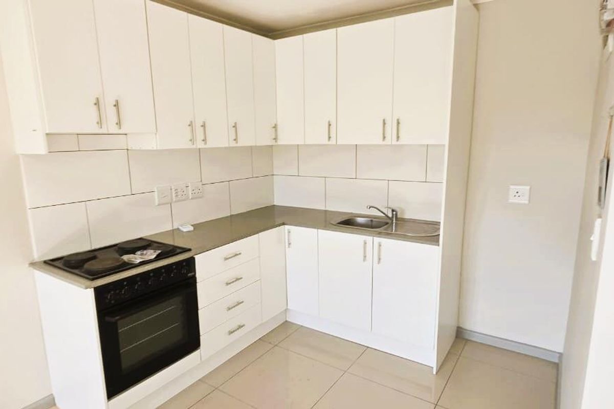 A clean, modern kitchen featuring white built-in cabinetry, a stainless steel sink, and an integrated electric oven and hob with a tiled backsplash.