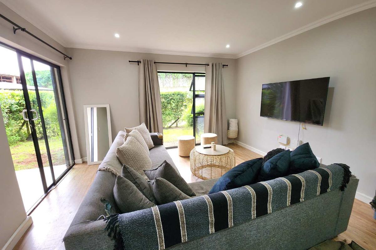 A bright and modern living room featuring laminate flooring, recessed downlights, and large sliding glass doors providing direct access to the garden.
