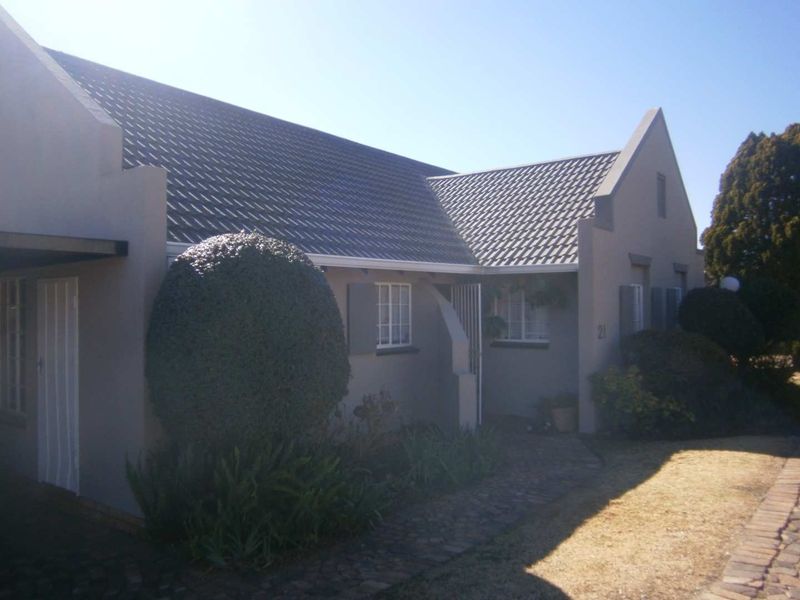 Front elevation of a townhouse featuring a gabled tiled roof, paved walkway, and established garden landscaping.