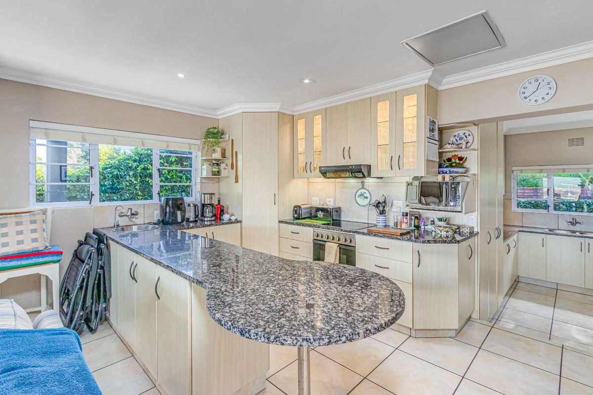 A functional kitchen featuring granite countertops, light wood cabinetry, a built-in oven, extractor fan, and a breakfast bar, with an adjacent scullery area.