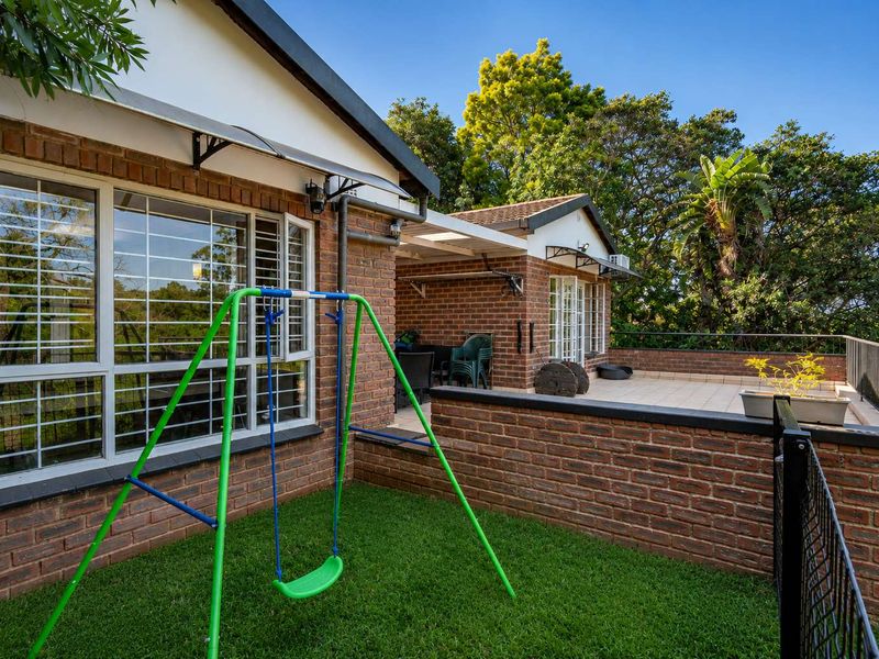 A rear exterior view of the townhouse featuring a face brick facade, a paved patio area, and a small private garden space.