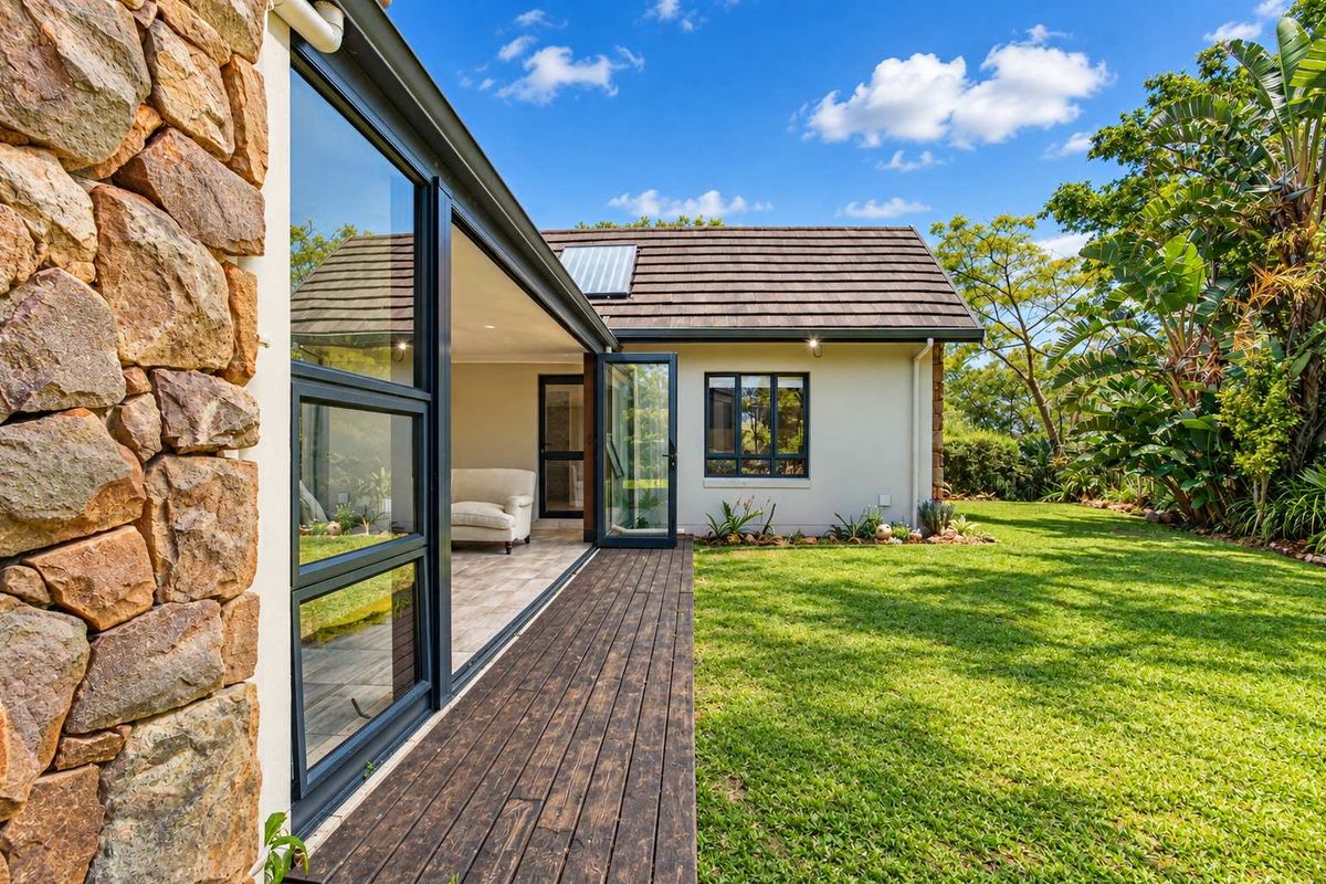 A well-maintained rear exterior featuring stone cladding, timber decking, and bi-fold doors opening onto a lush green garden.