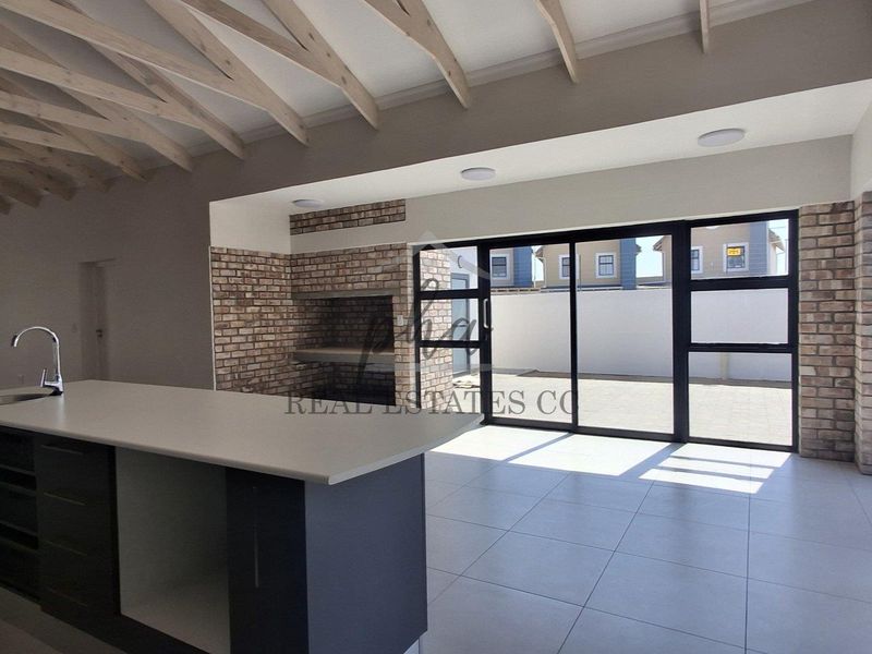 Spacious open-plan living area featuring exposed timber rafters, a built-in brick fireplace, and a modern kitchen island with direct access to the patio.