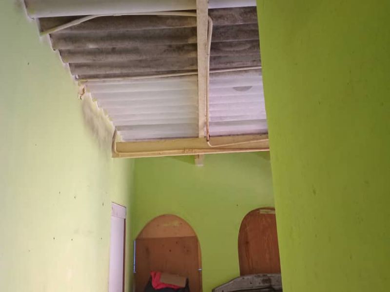A bedroom space featuring exposed corrugated roofing and arched doorways, requiring significant renovation to improve structural finishes and overall condition.