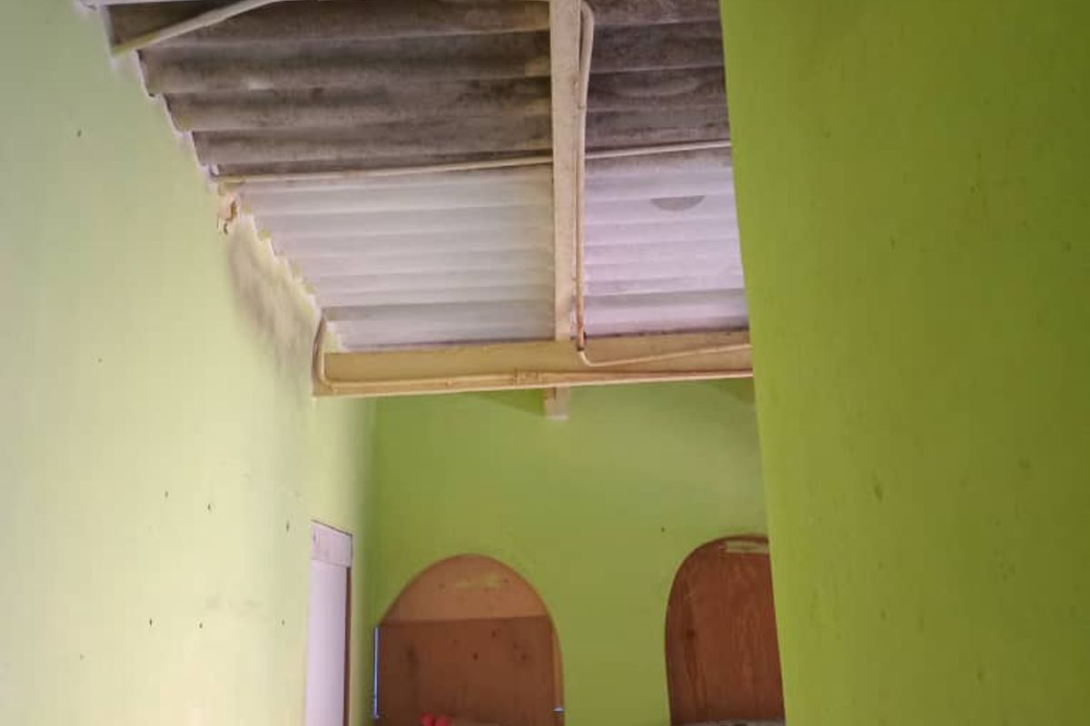 A bedroom space featuring exposed corrugated roofing and arched doorways, requiring significant renovation to improve structural finishes and overall condition.