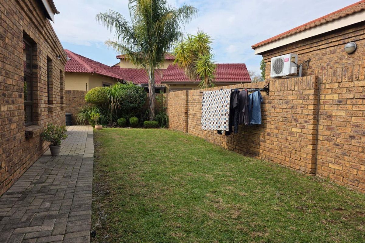 A private rear garden featuring a paved walkway, lawn area, and brick boundary walls with an integrated wall-mounted air conditioning unit.
