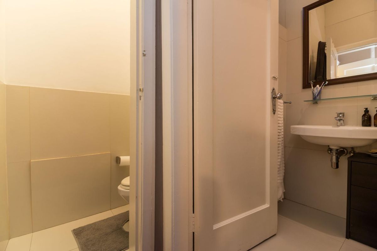 A functional bathroom featuring a wall-mounted basin, mirror, and a separate toilet area with neutral wall tiling.